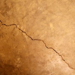 Brown and tan stained image of cracked cement. Does Home Insurance Cover Foundation Work? What Can You Do If It Doesn't?